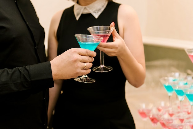 A man and a girl hold glasses with blue and pink cocktails in their hands