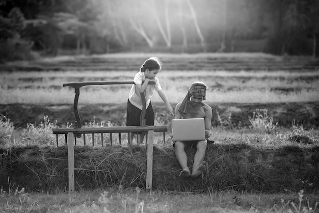 A man and a girl sit on a fence with a rake and a tractor.