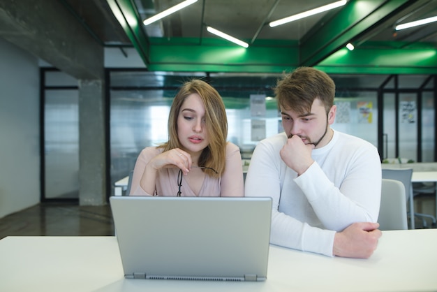 A man and a girl sitting in a modern office at the table and looking at a laptop.