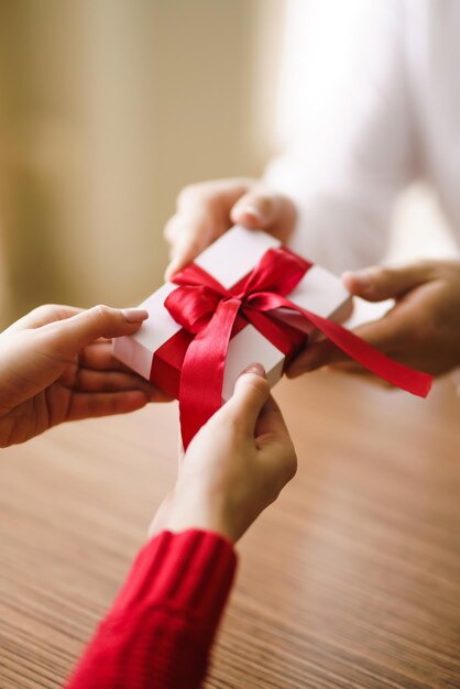 Man gives to his woman a gift box with red ribbon Hands of man gives surprise gift box for girl