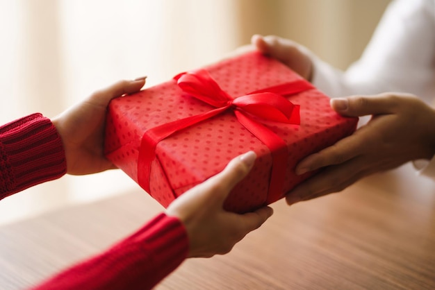 Man gives to his woman a gift box with red ribbon hands of man\
gives surprise gift box for girl