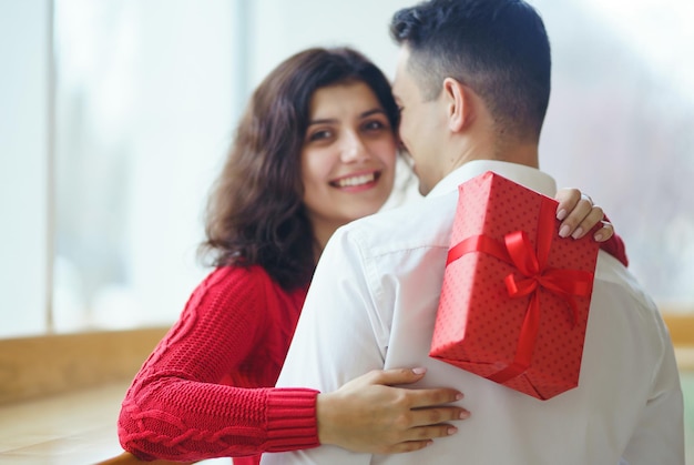 L'uomo dà alla sua donna una confezione regalo con nastro rosso una coppia di innamorati che celebra il giorno di san valentino