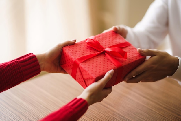 사진 남자는 그의 여자에게 빨간 리본으로 선물 상자를 준다 남자의 손은 여자를 위한 깜짝 선물 상자를 준다