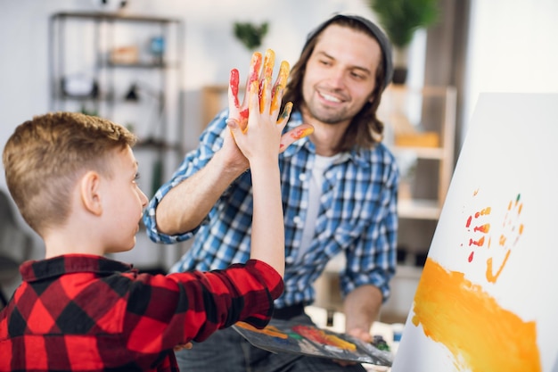 Foto uomo che dà il cinque al figlio mentre dipinge sul cavalletto
