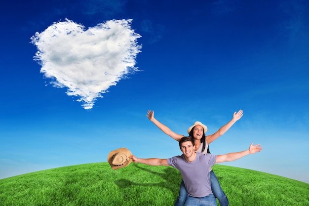 Man giving his pretty girlfriend a piggy back against cloud heart