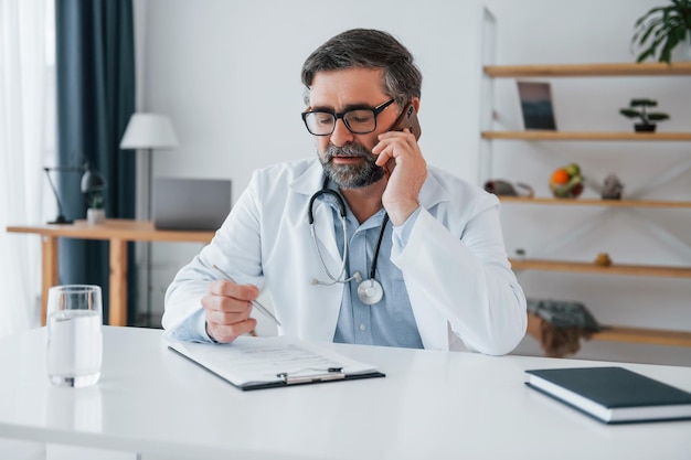 Man giving information by phone professional medical worker in\
white coat is in the office