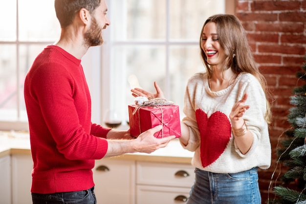 Man giving a New Year gift for a young excited woman standing near the Christmas tree at home