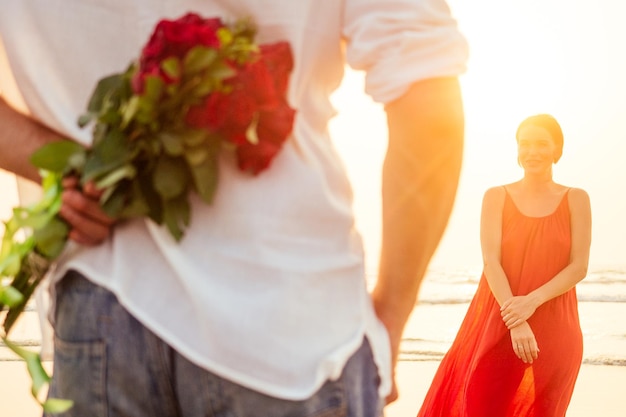 Man giving roses to his surprise and wonder woman on the ocean beach. romantic date or wedding or valentines day concept by sea.loving couple celebrating March 8 Women's Day and happy birthday