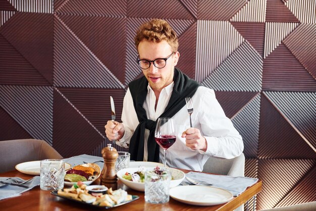 Photo man in glasses sits by the table indoors of new modern luxury restaurant