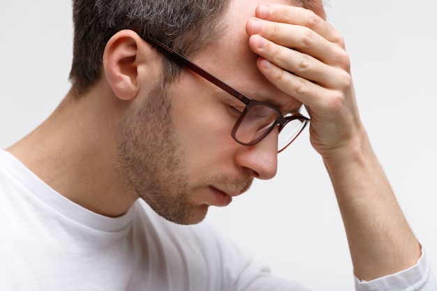 Man in glasses in white top touching his forehead, feels tired after work