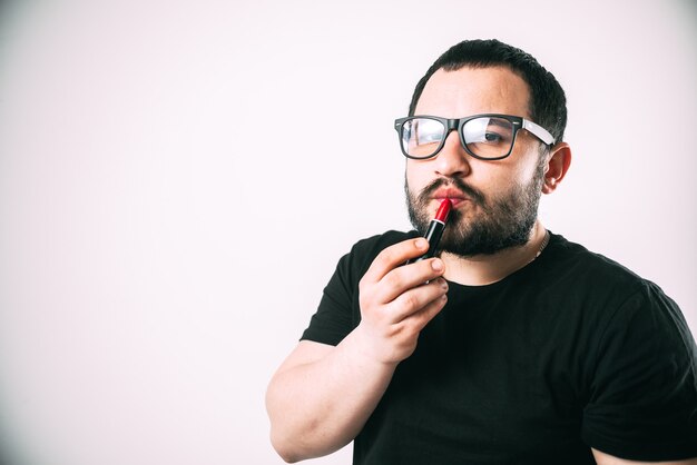 a man in glasses with a beard paints his lips with red lipstick