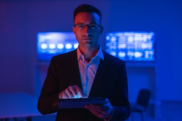 The man in glasses with a tablet working in a room with screens