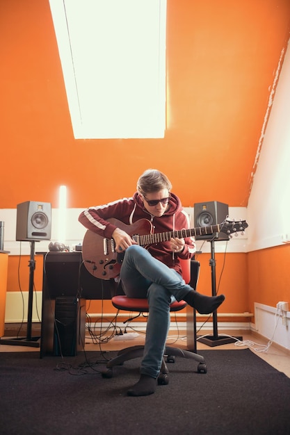 A man in glasses working in the studio playing guitar