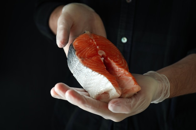 Man in gloves hold salmon meat on dark surface