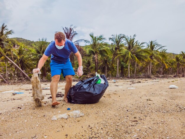 Man in gloves pick up plastic bags that pollute sea Problem of spilled rubbish trash garbage on the beach sand caused by manmade pollution campaign to clean volunteer in concept