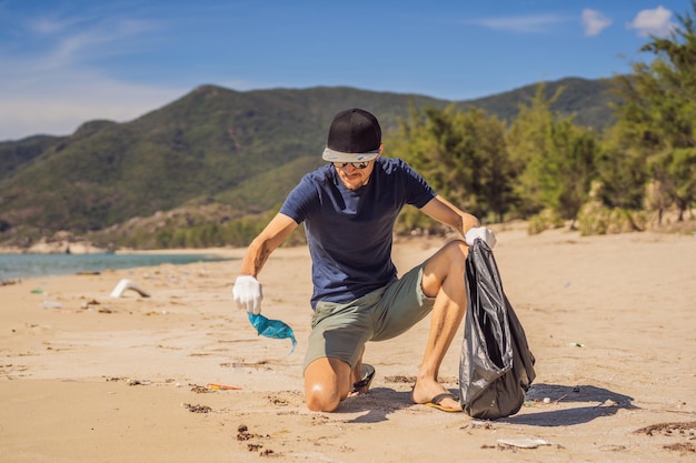 Photo man in gloves pick up plastic bags that pollute sea problem of spilled rubbish trash garbage on the beach sand caused by manmade pollution and environmental campaign to clean volunteer in concept