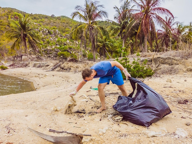 Man in gloves pick up plastic bags that pollute sea Problem of spilled rubbish trash garbage on the beach sand caused by manmade pollution and environmental campaign to clean volunteer in concept