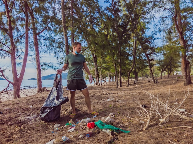 手袋をはめた男が海や森を汚染するプラスチックを拾う人為的な汚染キャンペーンによって引き起こされた砂浜にゴミがこぼれるという問題