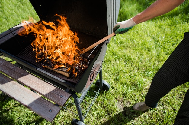 Un uomo in guanti raddrizza legna ardente nella griglia. barbecue estivo