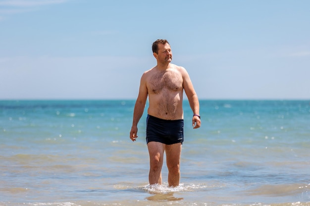 Мужчина выходит после купания на берег моря на летние каникулы