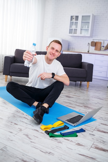 남자는 집에서 스포츠를 하러 간다. 운동선수는 집에서 바닥에 앉아 물을 마신다, 건강한 생활 방식