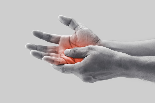 Un uomo afferra il palmo della mano perché il palmo della mano è stato ferito dolore alla mano su uno sfondo grigio