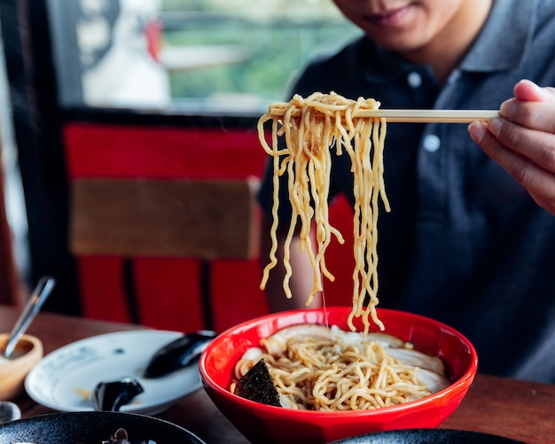 남자는 Shoyu Chashu Ramen의 젓가락으로 그릇에서라면을 손으로 잡아냅니다.