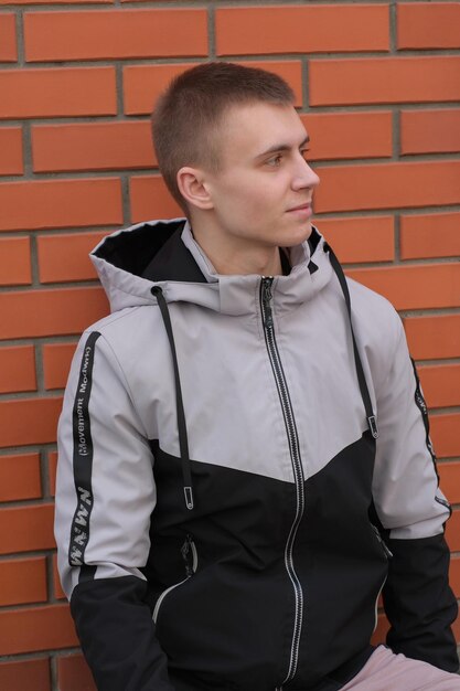 A man in a gray and black hoodie stands against a brick wall.