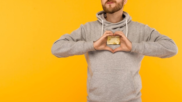 Man in a gray hoodie holds a credit card in his hands on a yellow background