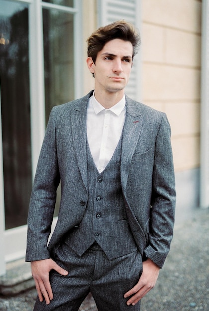 Man in a gray suit stands near the wall of an old villa with large windows