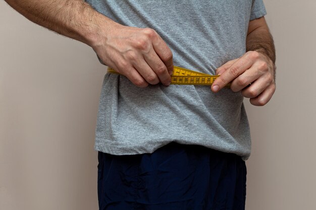 Man in a gray T-shirt measuring the waist