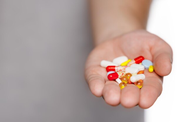 Man in gray tshirt hold pile of various colorful multicolored pills in hand Medicines vitamins antibiotics and medicaments Selective focus Copy space First aid treatment and healthcare concept