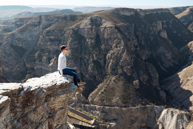 Man in a gray turtleneck and sunglasses sits over a cliff