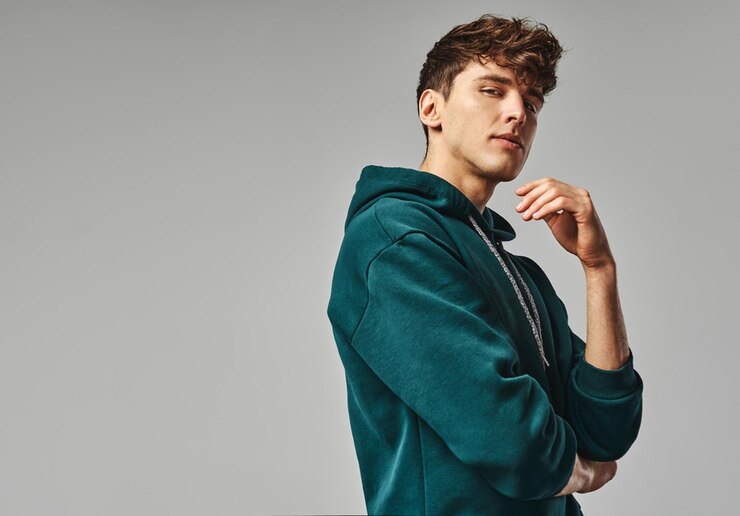 Photo a man in a green hoodie stands in front of a gray background