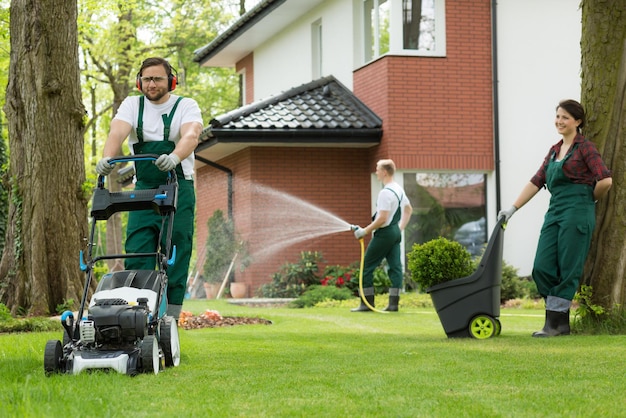 A man in green overalls is using a lawnmower to clean the lawn.