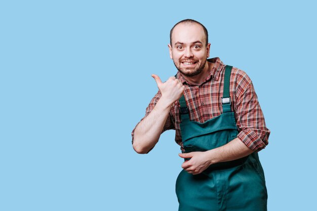 Man in green overalls smiling and giving thumbs up against blue background