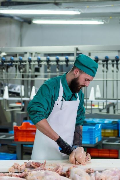 A man in a green scrubs cuts meat in a factory.