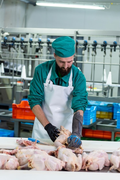 A man in a green scrubs cuts meat on a table.