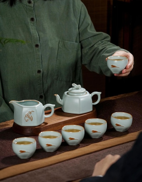 A man in a green shirt holds a cup of tea and cups of tea.