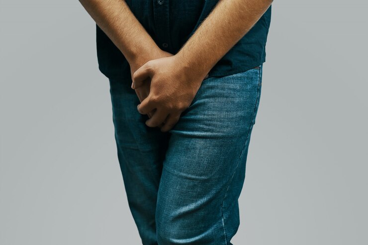 Man in a green shirt and jeans feels pain in the crotch hiding behind his hands 