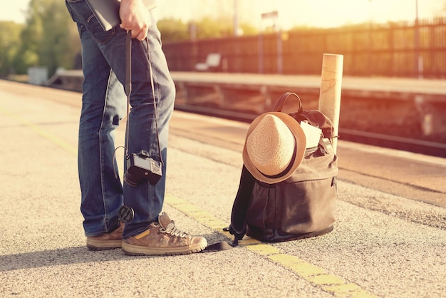 Человек и зеленый туристический рюкзак шляпа карты очки на платформе на вокзале на закате