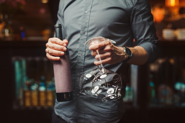 灰色のシャツを着た男は、おいしいワインとエレガントなきれいなメガネのボトルを保持します