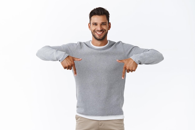 man in grey sweater, pointing fingers down and smiling, give advice where find good product, promote application or store banner