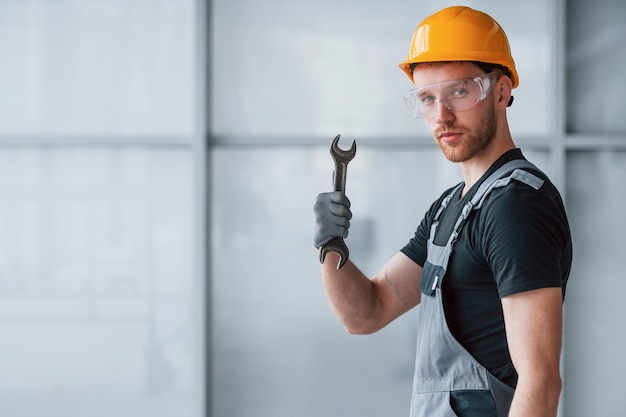 Man in grey uniform with wrench in hand standing indoors in
modern big office at daytime