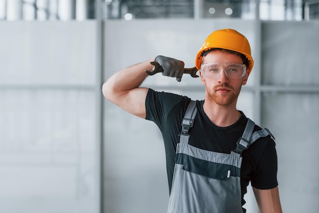 Man in grey uniform with wrench in hand standing indoors in modern big office at daytime