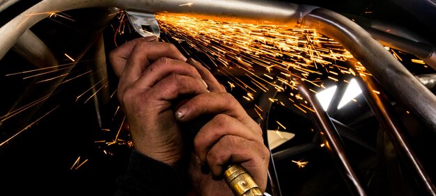 Uomo che macina tubi d'acciaio con un disco di macinazione pneumatico caldo che fa scintille