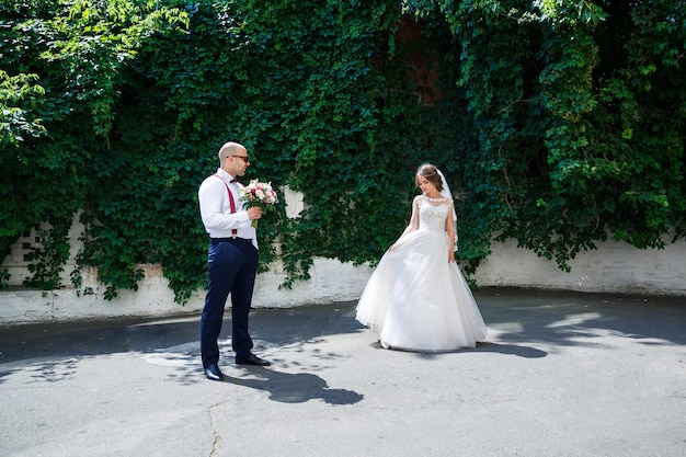 Sposo dell'uomo in camicia bianca e pantaloni, una bella sposa in abito bianco e velo, in posa e camminando lungo la strada il giorno del matrimonio