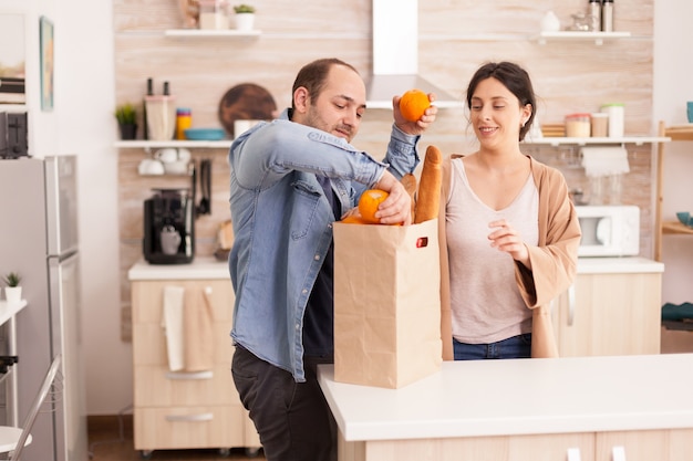 Man haalt sinaasappels uit de boodschappentas in de keuken met zijn vrouw. Gezonde gelukkige relatie-levensstijl voor man en vrouw, samen winkelen producten