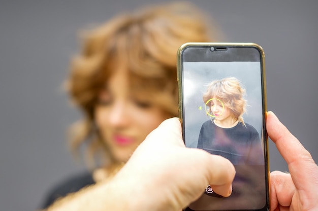 Man hairdresser taking pictures on the smartphone of her client's hairstyle against a gray background