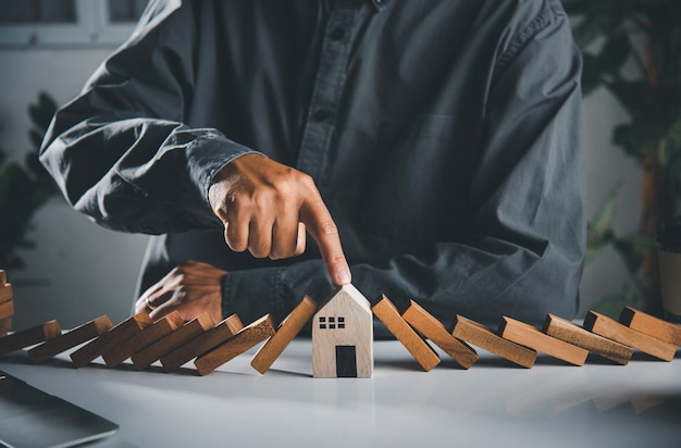 Man hand blocks wood block from many row falling wooden block like domino to house model